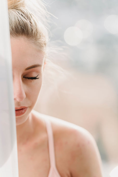 Woman sitting by a sunlit window with eyes closed, taking a slow, calming breath — the regulated state The Somatic CBT Workbook trains